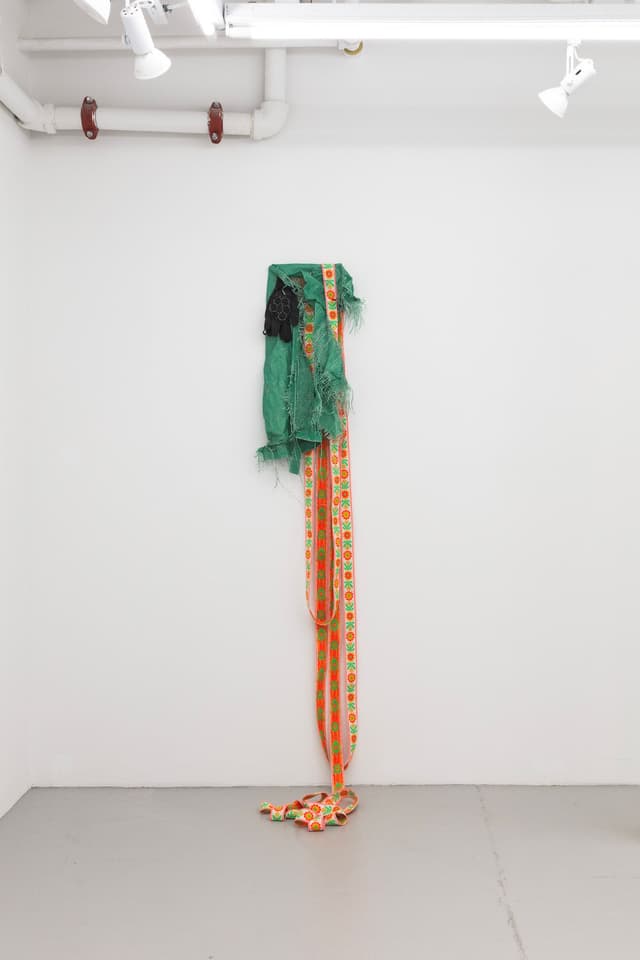 Jeneen Frei Njootli. Lisa, 2022. Green Tarp, gloves, staples, ribbon, plywood. 30 x 18 x 3 inches / Variable upon installation.