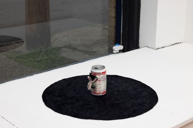 Audie Murray. <i>Bud, Tobacco & Spider</i>, 2021. Budweiser beer can, silver thread, tobacco bundle, black velvet. 5 × 18.5 × 18.5 inches.