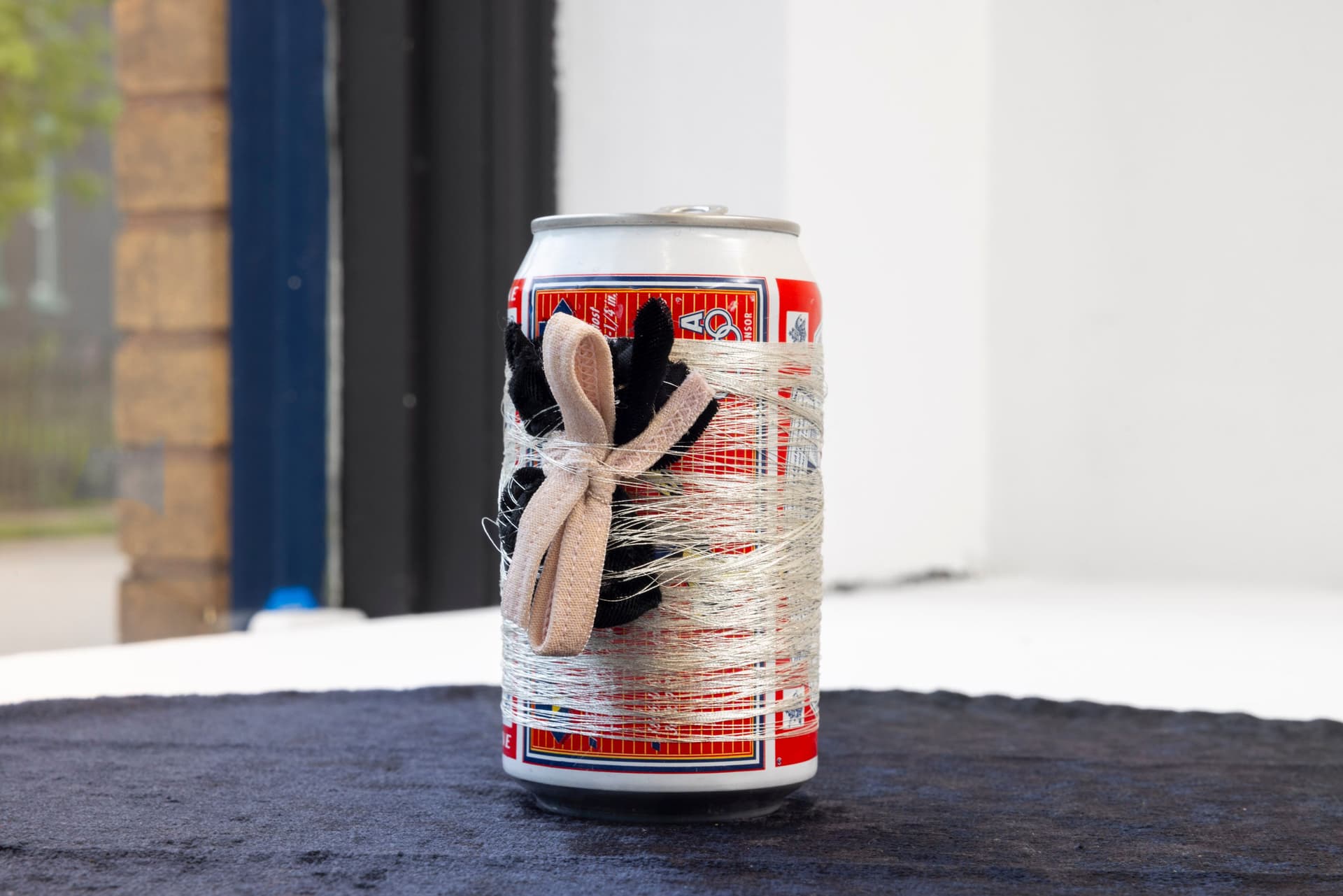 Audie Murray. Detail of <i>Bud, Tobacco & Spider</i>, 2021. Budweiser beer can, silver thread, tobacco bundle, black velvet. 5 × 18.5 × 18.5 inches.