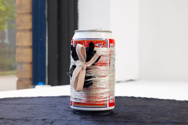 Audie Murray. Detail of <i>Bud, Tobacco & Spider</i>, 2021. Budweiser beer can, silver thread, tobacco bundle, black velvet. 5 × 18.5 × 18.5 inches.