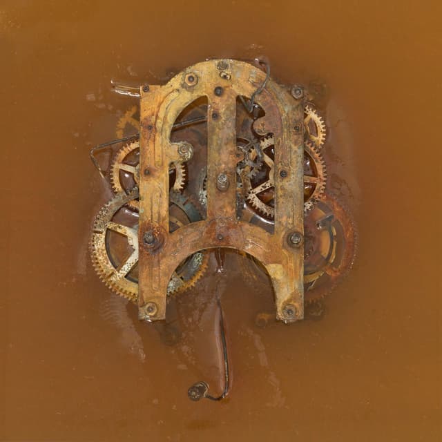 Micah Schippa. The last sentence ever written (Detail), 2024. Brass clock movement mechanism in gastric solution (HCL solution made to mimic the composition of stomach acid), plexiglass vitrine. 15 x 15x 15 inches.